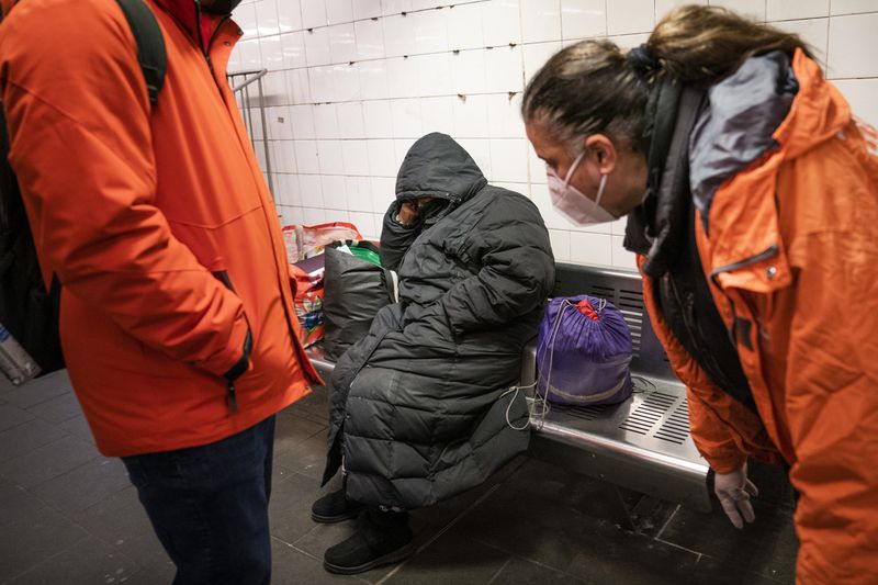 Homeless Outreach Personnel reach out to a person sleeping on a bench in the Manhattan subway system